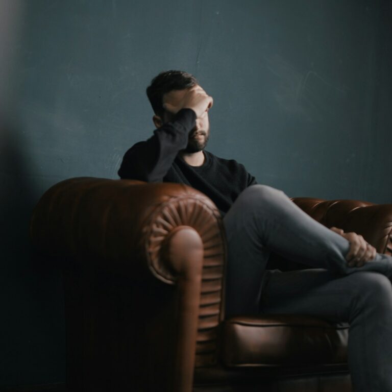 a man holds his head while sitting on a sofa